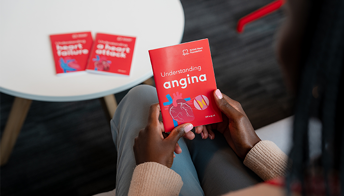 Someone holding a small red booklet that says Understanding angina, with 2 more booklets in the background