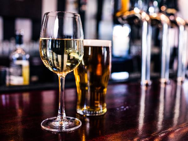 a glass of white wine and a pint of beer sitting on top of a bar in a pub