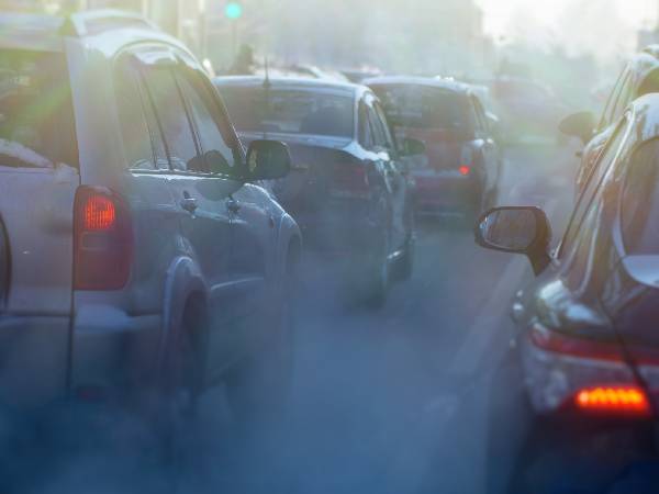 cars stuck in a traffic jam with lots of grey smoke coming out of their exhaust pipes