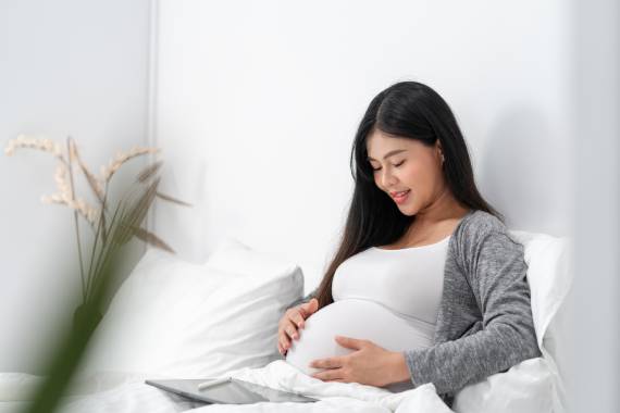 a smiling woman sitting on a sofa and staring down at her pregnancy bump
