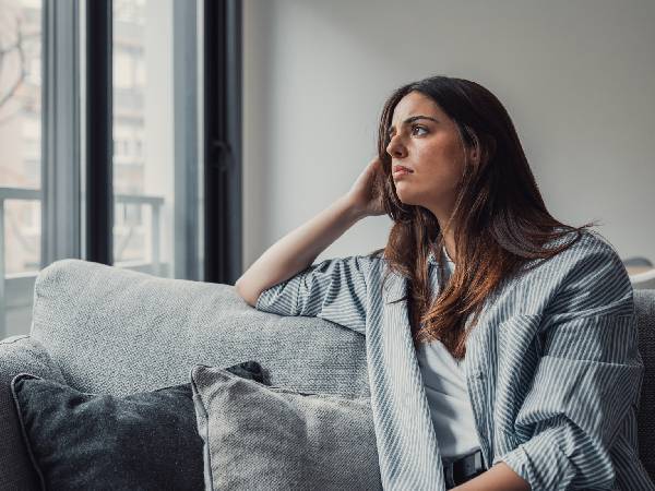 a woman sitting on a sofa and staring out of her window with a worried expression on her face