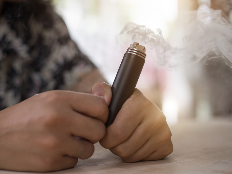 Someone sitting at a table and holding a vape.