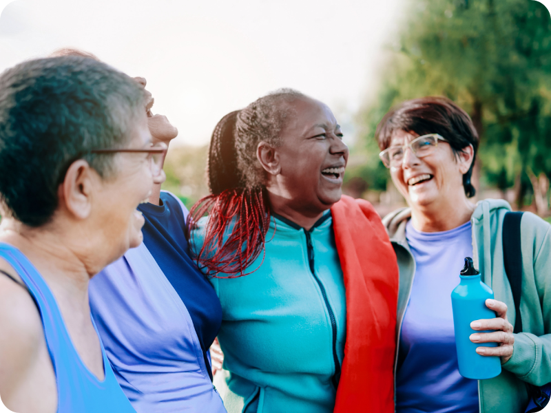 A group of women in gym clothes laugh together in a park.