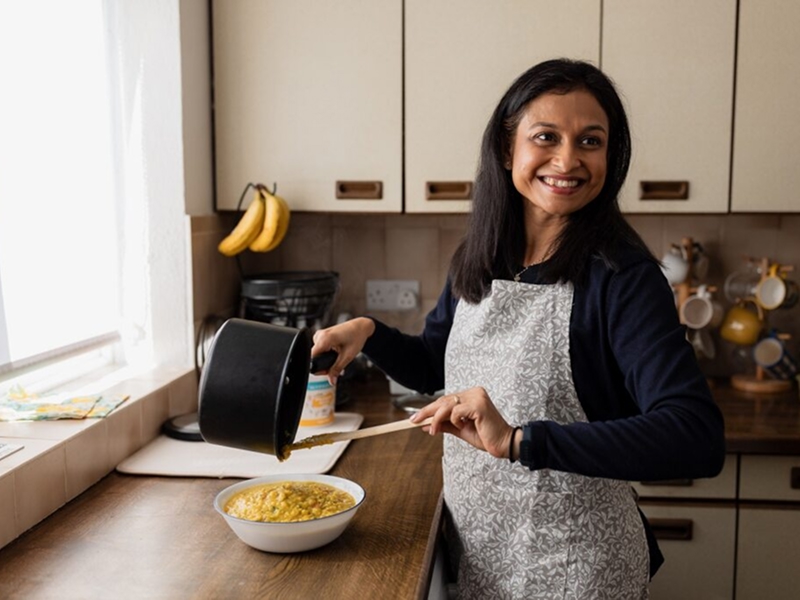 Puloma, who lowered her cholesterol with lifestyle changes. She is in a kitchen cooking and smiling. 