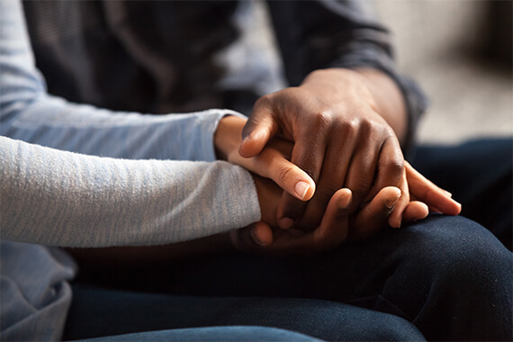 close up of two people holding hands over their knees whilst sitting down