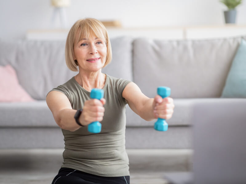 A white woman holding dumbbells in her home.