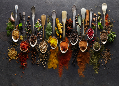 10 spoons with different herbs and spices on each against a dark background.
