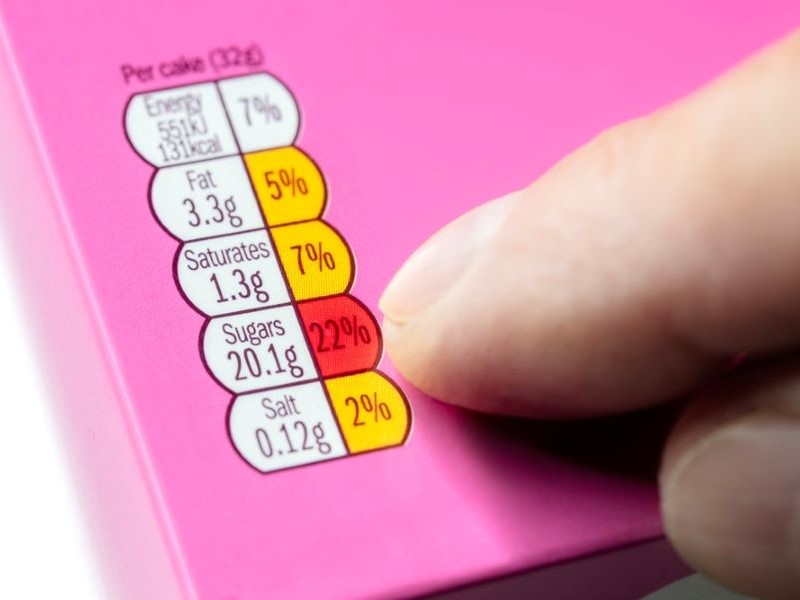 Close up of traffic light nutrition labelling on a pink box, with an index finger pointing to it.