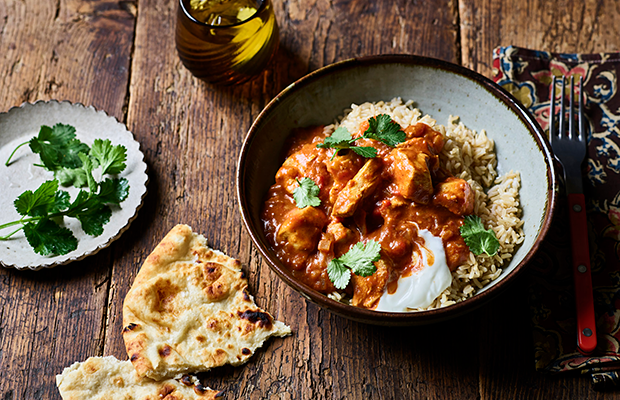 orange-red Chicken tikka masala with rice and garnished with low-fat Greek-style yogurt and coriander leaves. Presented on a wooden table with wholemeal chapati.