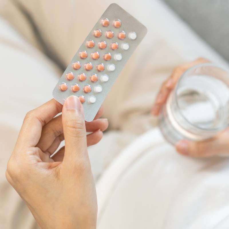 Hand holding a pack of contraceptive pills and a glass of water 