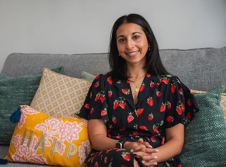 a young woman of South Asian heritage sitting on a sofa and smiling