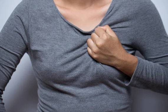 a close up image of a woman in a grey shirt clutching the left side of her chest
