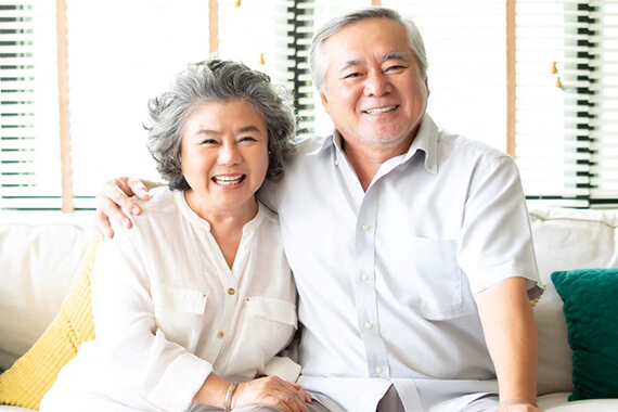 Two adults sit next to each other smiling on the sofa holding the other person's shoulder and thigh