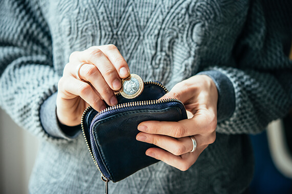 a person holds a coin above a navy blue purse