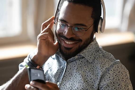 a young black man wearing glasses and headphones smiling as he looks down at his mobile phone