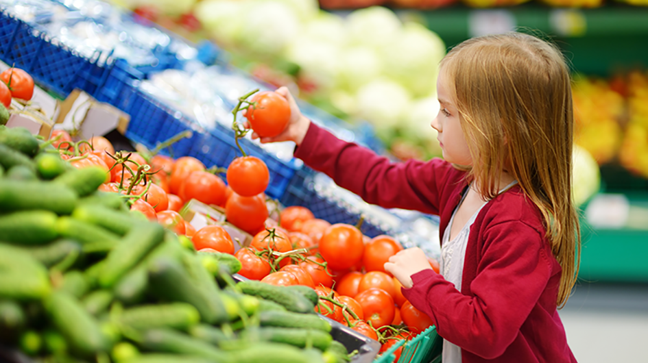 Little girl reaching for a tomato in a supermarket