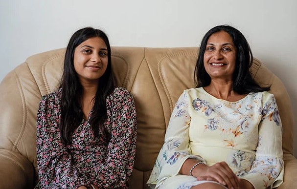 Two women sat together on a brown sofa smiling