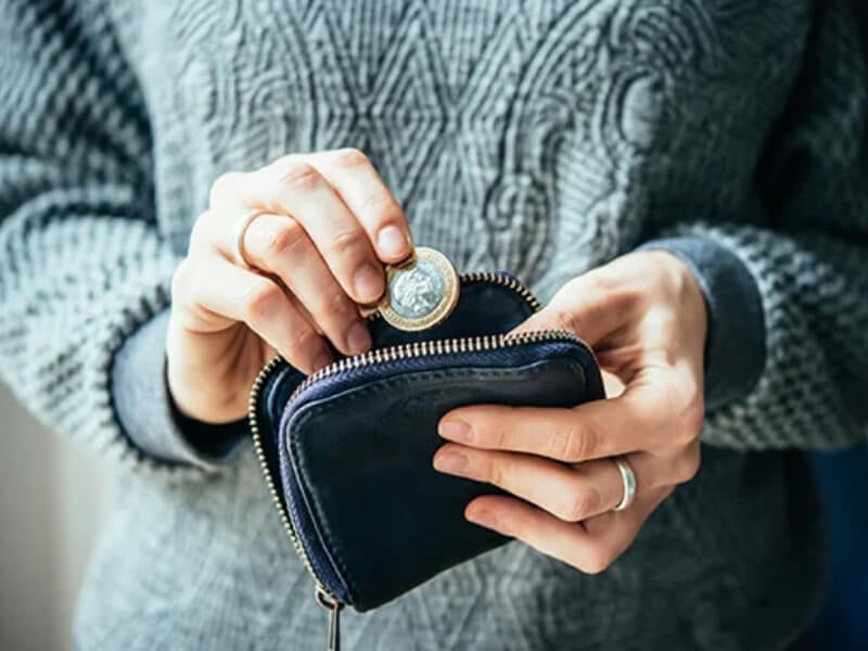 A woman putting a one pound coin into a purse