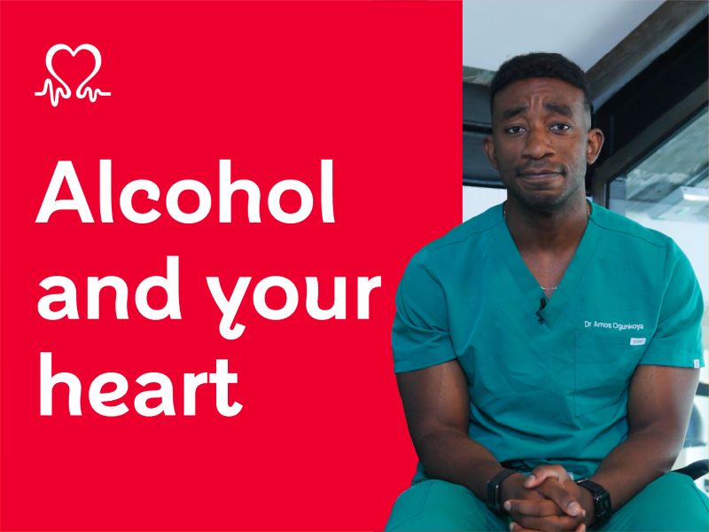 Man in scrubs sat down and facing the camera. On the left is a block red background with white text that says 'Alcohol and your heart'