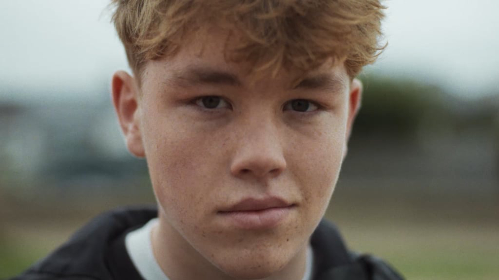 A young boy sat on a red bench looking forward