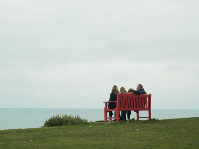 A family sat on a red bench overlooking the sea