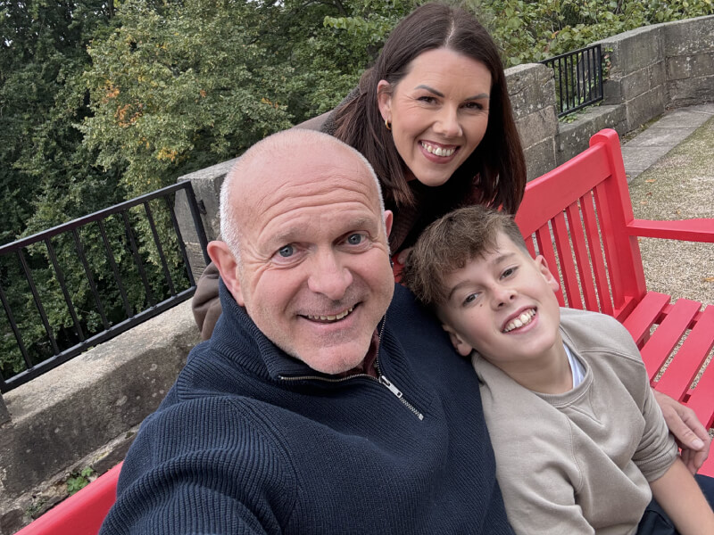 Dean smiling and sitting on a red bench with his wife and son