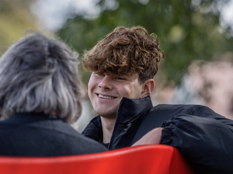 Jack sat on a red bench smiling at someone sitting next to him