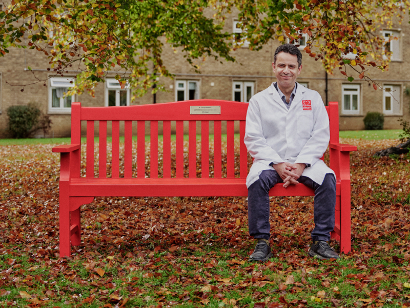 Professor Charalambos Antoniades sitting on a red bench smiling