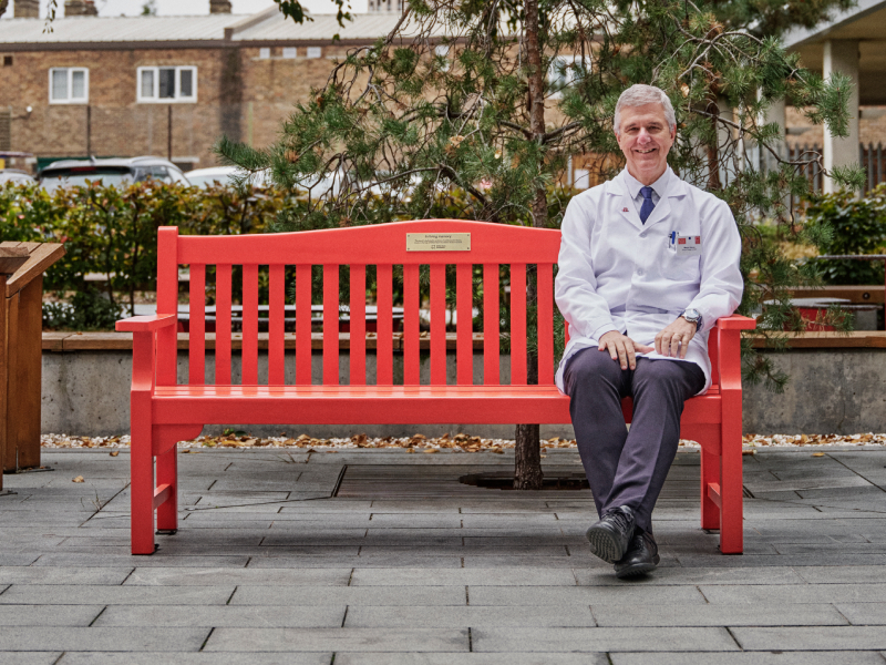 Professor Mauro Giacca sitting on a red bench smiling