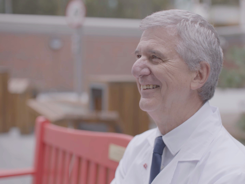 Professor Mauro Giacca sitting on a red bench smiling