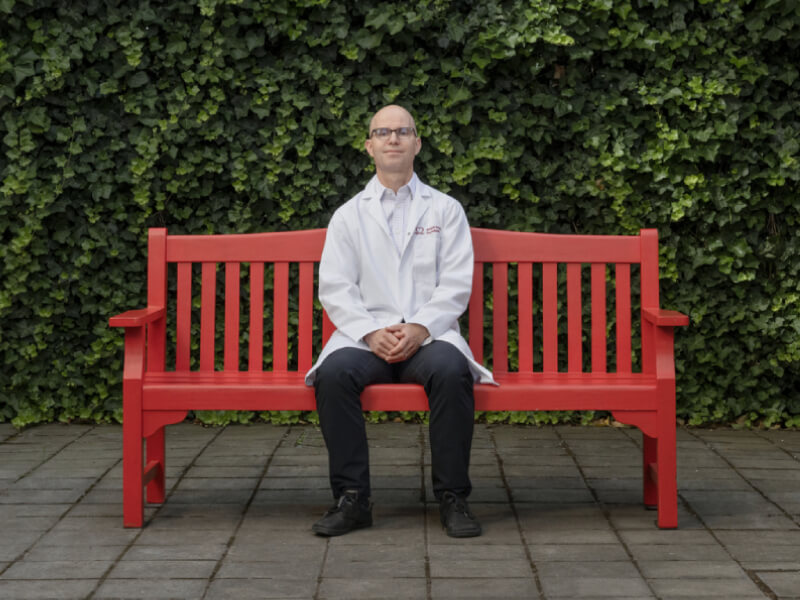 Dr Zachary Whinnett sat on a red bench smiling