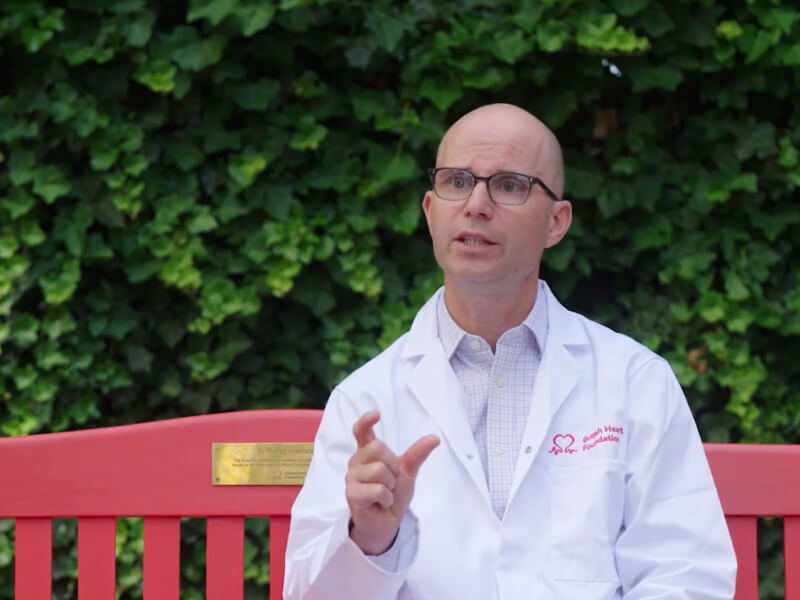 Dr Zachary Whinnett sat on a red bench talking about the smart T-shirt he is developing to help detect hidden heart rhythm conditions