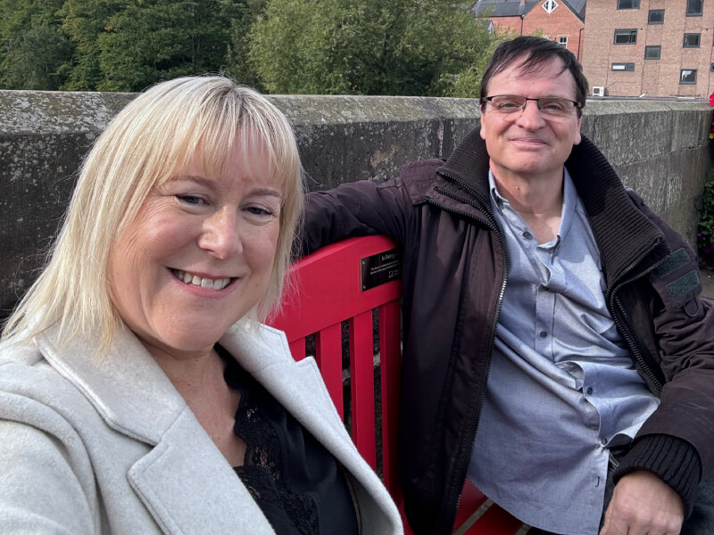 Louise and husband Bryan, sitting on a red bench for BHF's Keep us Beating campaign.
