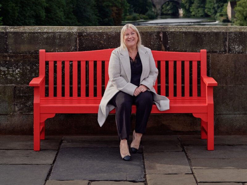 Louise is sitting on a red BHF bench for our Keep us Beating campaign.