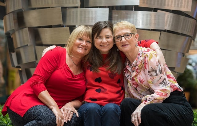 A trio of women smiling together in front of the Heart of Steel
