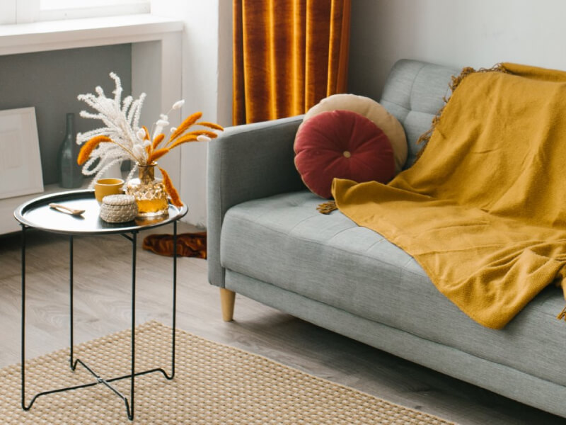 A living room with a grey sofa, red cushions and a yellow blanket draped over it and a circular coffee table
