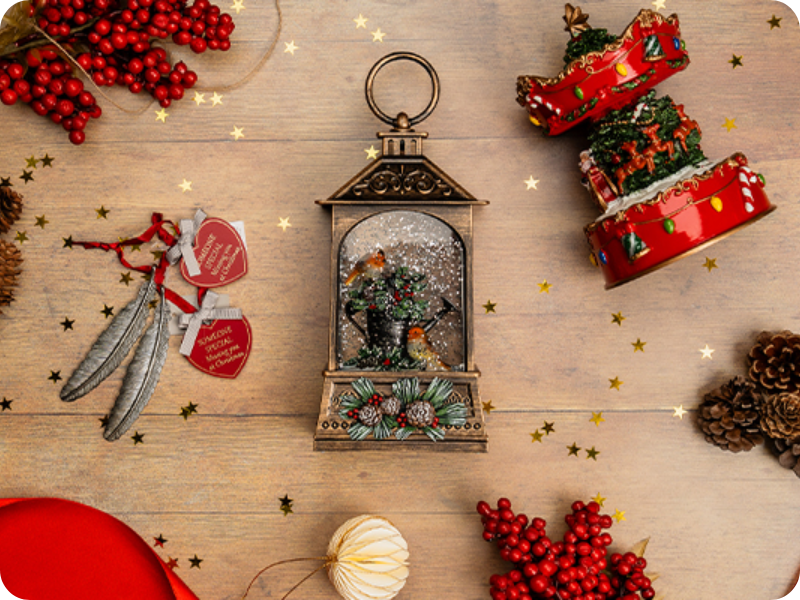 Christmas decorations arranged on a wooden surface, featuring a festive lantern, berry sprigs, pine cones, ornaments, and holiday trinkets.