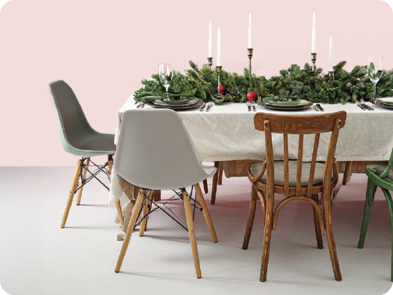 Festive dining table set with greenery, candles and place settings, surrounded by mixed wooden and modern chairs.