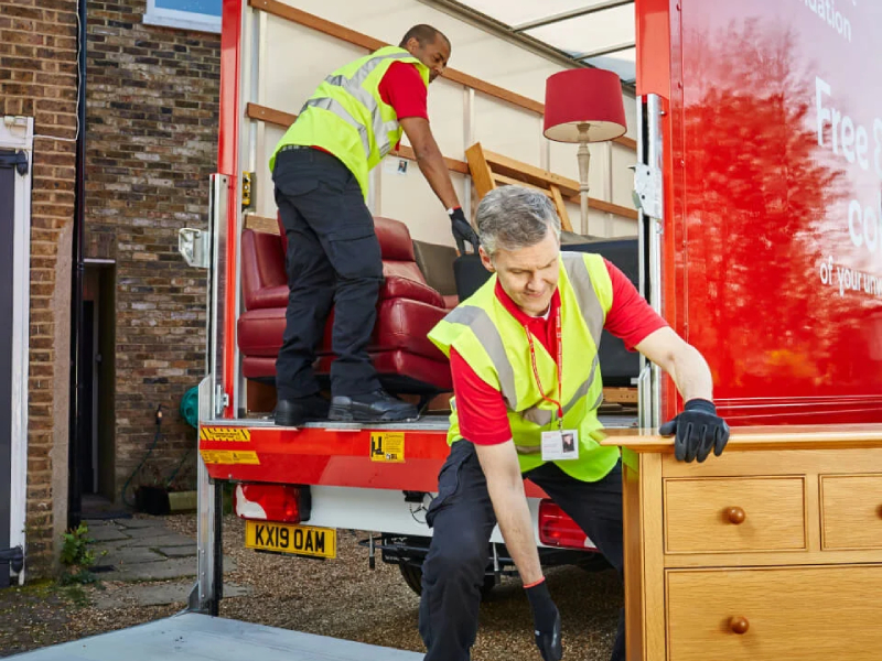Two men wearing hi vis jackets moving furniture into a van