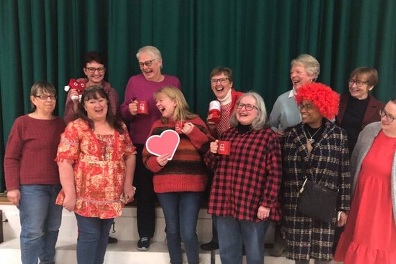 A group of people smiling and dressed in red inside a community hall as they hold British Heart Foundation mugs and collection tins