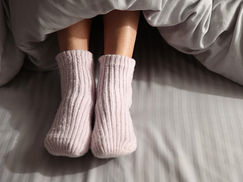 woman wearing thick pink socks under duvet