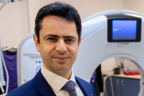 A male professor wearing a suit and standing beside an MRI scanner