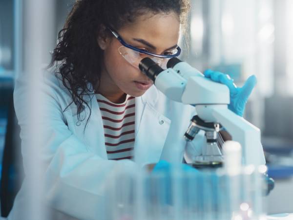 a young female scientist sitting in a lab and staring through a microscope