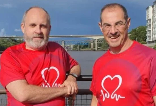 Two men in BHF branded t shirts standing in front of a river and smiling at the camera