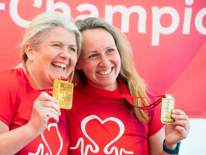 Two women in BHF branded t-shirts smiling while holding up gold medals