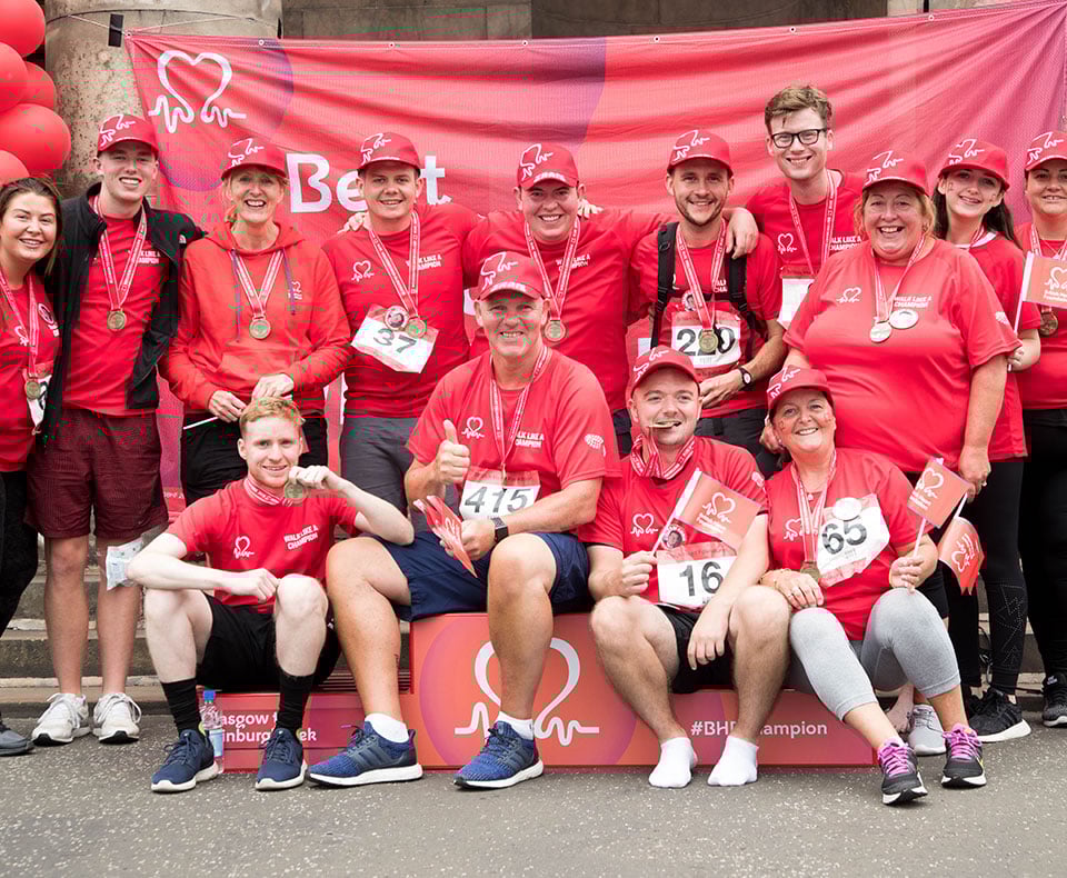 Group of BHF supporters smiling and wearing medals as they sit and stand around a podium