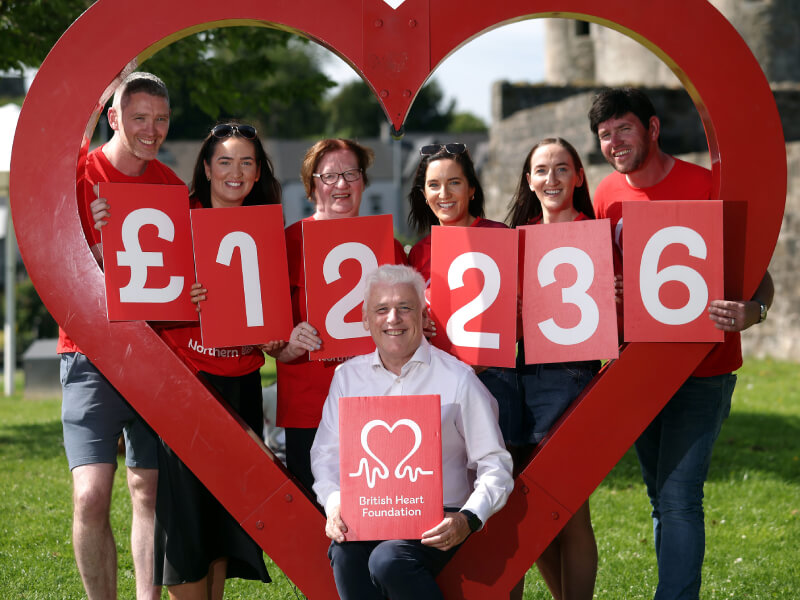 Group of supporters hold up numbers reading £12,236, surrounded by a red heart sculpture. 