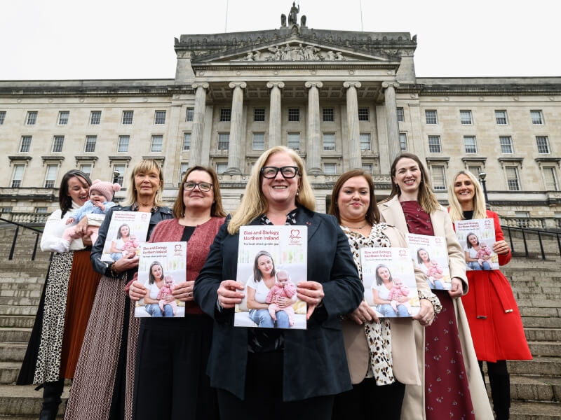 A group of supporters stand outside a parliamentary building, each holding a BHF report in their hands.  