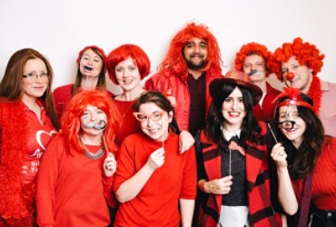 A group of fundraisers are wearing red shirts and smiling while they pose for a photograph