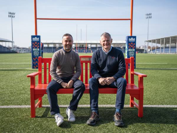 two men sitting on a BHF bench in a rugby field